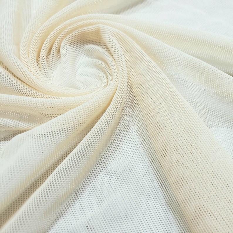 Pu&ograve; includere: Primo piano di un tessuto a rete color crema con un motivo testurizzato a griglia. Il tessuto &egrave; piegato e drappeggiato, creando curve e pieghe morbide.