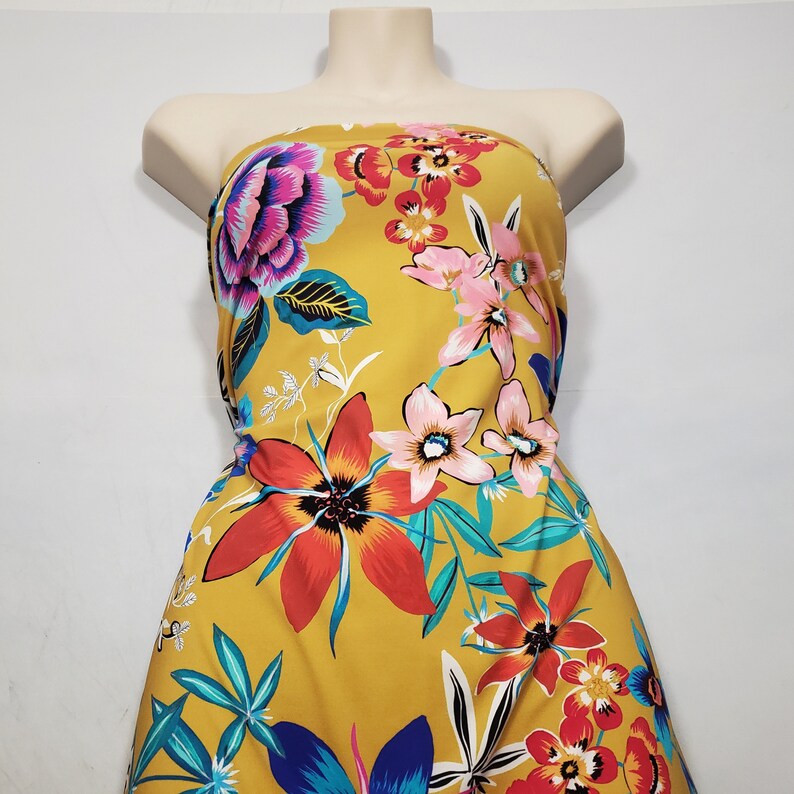 May include: Yellow fabric with a floral print featuring red, pink, blue, and green flowers. The fabric has a tropical theme.