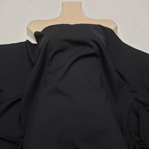 May include: A large piece of black fabric draped over a mannequin torso. The fabric is smooth and appears to be a solid color, with soft folds and shadows. The material is likely used for clothing or other textile projects.