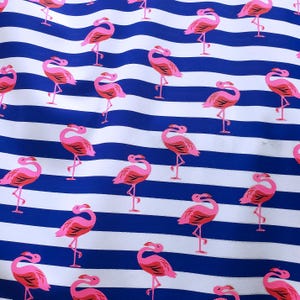 May include: A fabric with a repeating pattern of pink flamingos on a blue and white striped background. The flamingos are in various poses, with their long necks curved and their legs extended. The stripes are horizontal and evenly spaced.