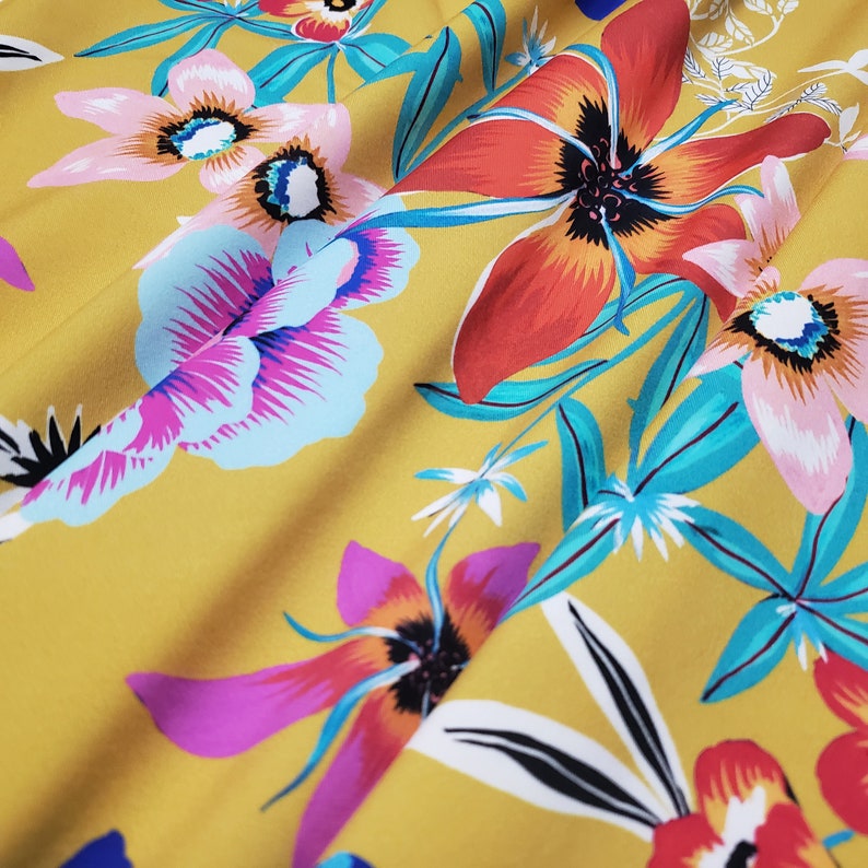 May include: A yellow fabric with a floral print featuring pink, red, blue, and white flowers. The fabric has a soft, flowing texture.