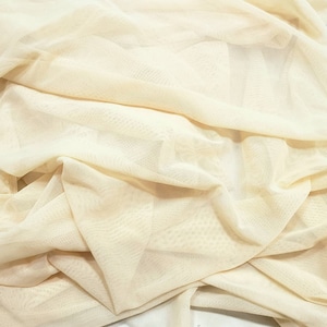 Pu&ograve; includere: Un primo piano di un tessuto beige trasparente con una trama a rete fine. Il tessuto &egrave; piegato e drappeggiato, mostrando la sua qualit&agrave; delicata e ariosa.