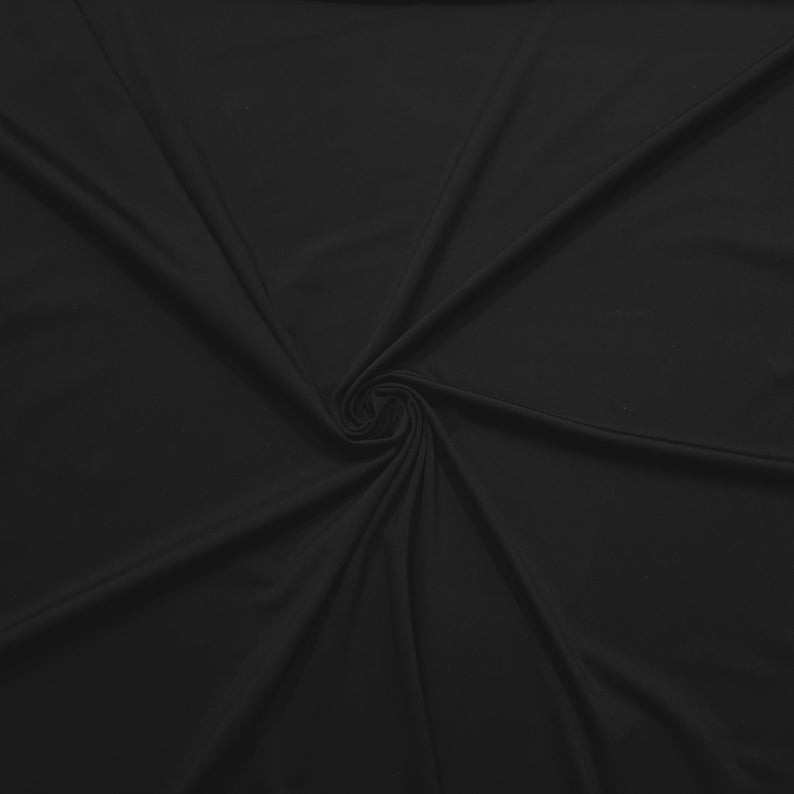 May include: A close-up shot of a black fabric with a smooth texture. The fabric is swirled in a circular pattern, creating a spiral effect in the center. The material appears soft and drapes in gentle folds, with subtle variations in light and shadow.
