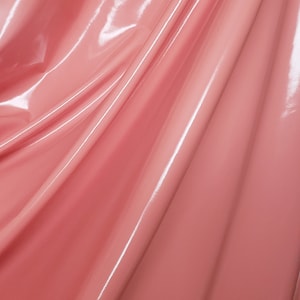 May include: A close-up of a smooth, shiny, pink fabric with a slight sheen. The fabric is folded and draped, creating soft curves and folds.