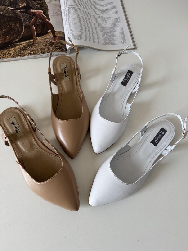 May include: Four pairs of women's slingback flats in neutral colors. Two pairs are a light tan, and two are white. Each shoe has a pointed toe and a thin strap around the ankle. The brand name "Klavels" is printed on a black label.
