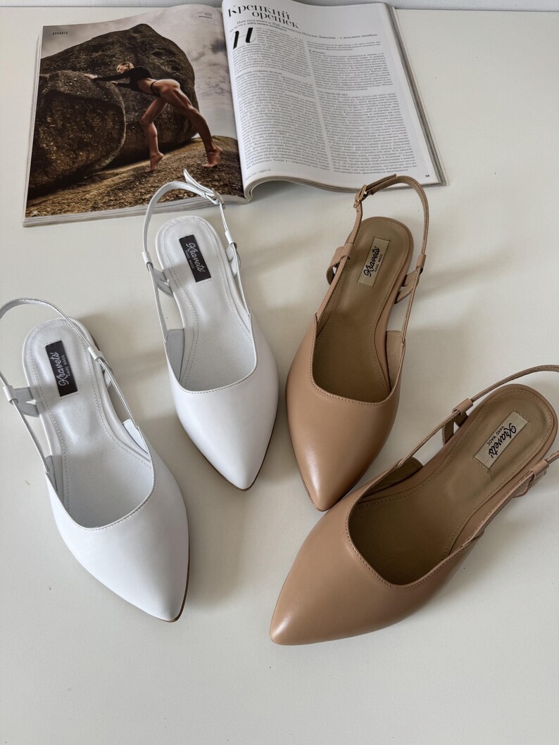 May include: Four pairs of women's slingback flats in white and tan leather. The shoes have pointed toes and adjustable ankle straps. The shoes are arranged on a white surface, with a magazine in the background.