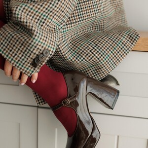 May include: Brown platform shoes with a buckle strap and a chunky heel. The shoes are made of patent leather and have a rounded toe.