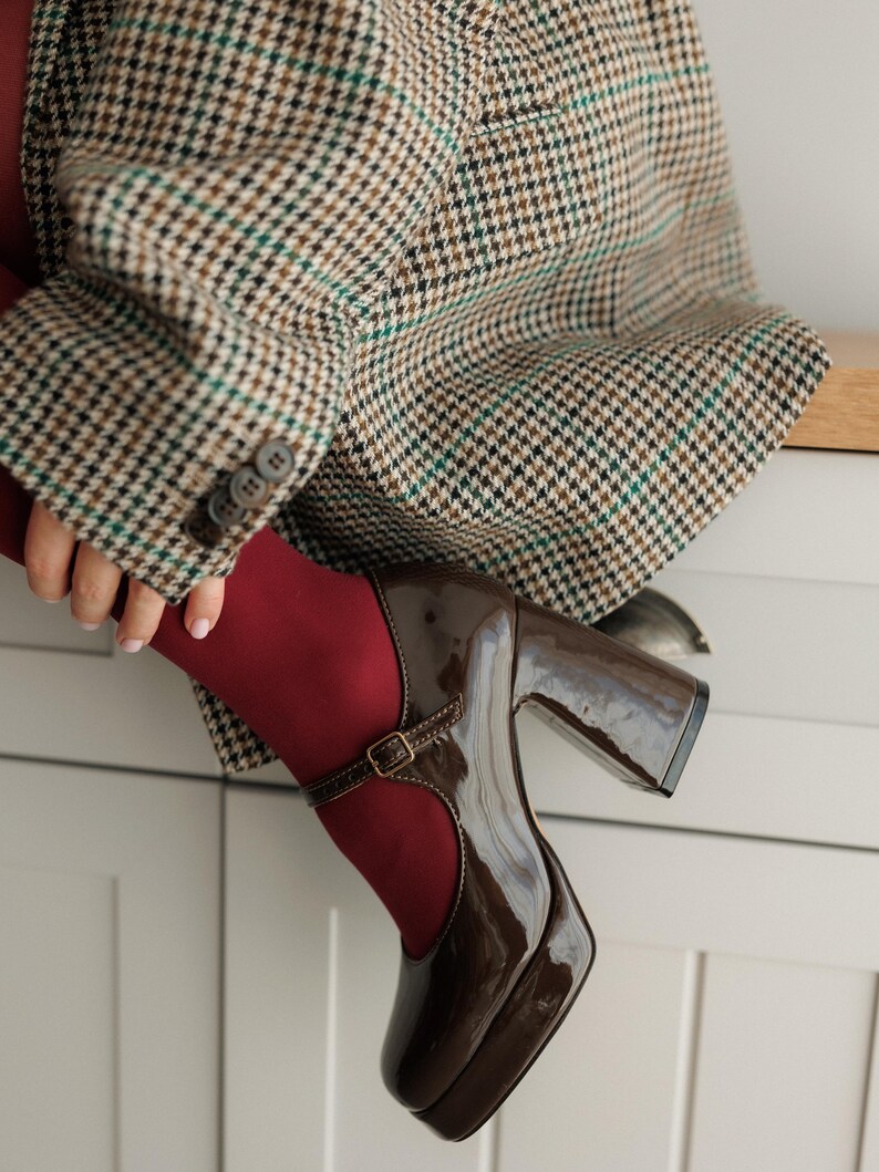 May include: Brown platform shoes with a buckle strap and a chunky heel. The shoes are made of patent leather and have a rounded toe.