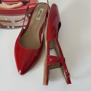 May include: Pair of red patent leather slingback flats with pointed toes. The shoes have a thin ankle strap with a small gold buckle and a small heel. The brand name "Kravets" is visible on the insole.