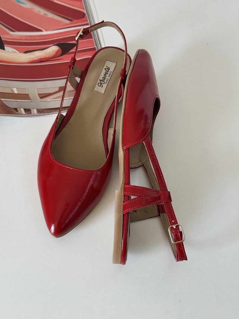 May include: Pair of red patent leather slingback flats with pointed toes. The shoes have a thin ankle strap with a small gold buckle and a small heel. The brand name "Kravets" is visible on the insole.