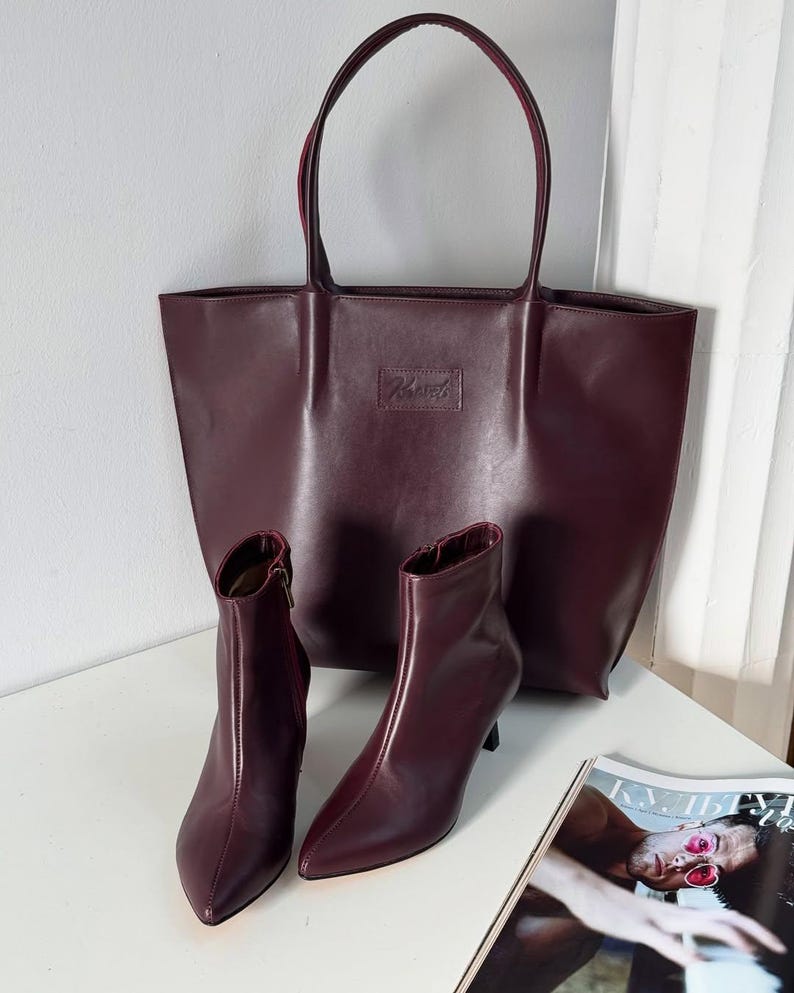 May include: A burgundy tote bag and matching ankle boots with pointed toes and stiletto heels. The bag has a rectangular shape with a small rectangular logo. A magazine is visible in the bottom right corner.
