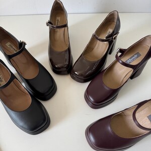 May include: Four pairs of women's platform shoes with buckle straps. The shoes are in black, brown, and burgundy leather. The shoes have a chunky heel and a square toe.