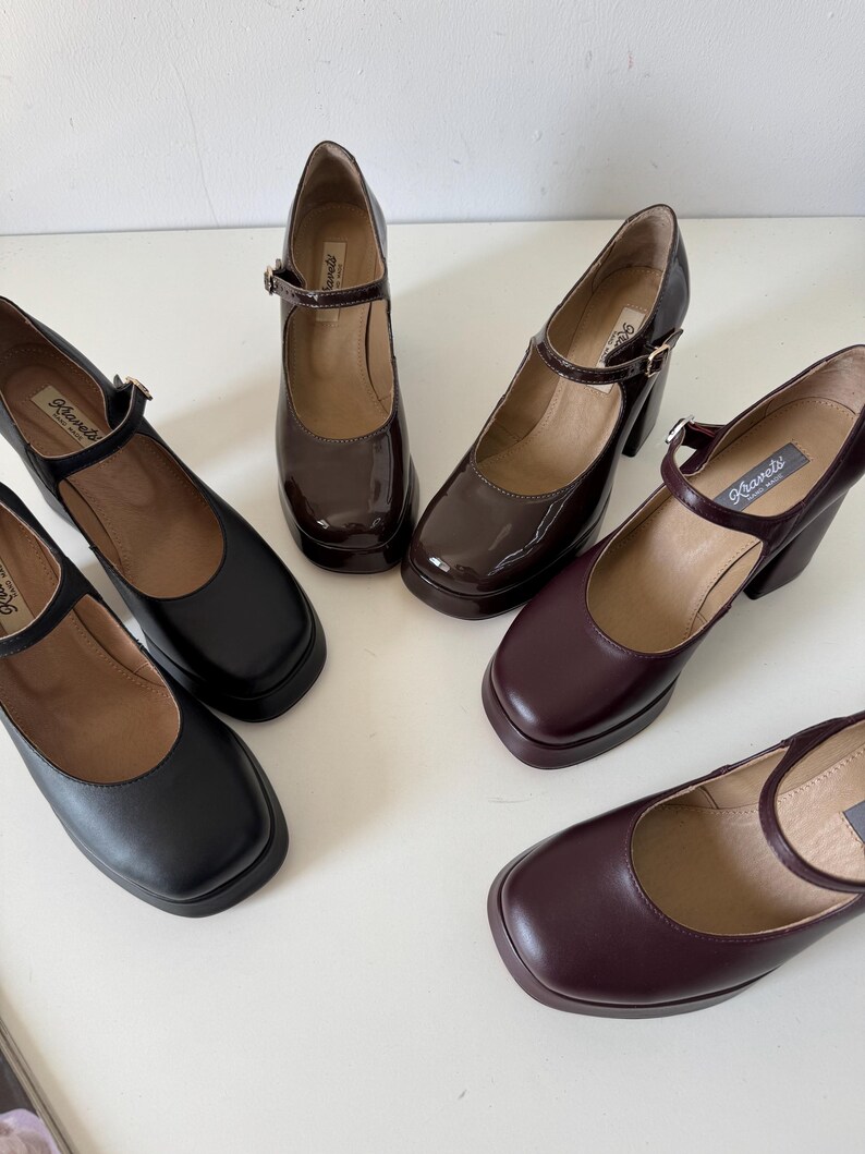 May include: Four pairs of women's platform shoes with buckle straps. The shoes are in black, brown, and burgundy leather. The shoes have a chunky heel and a square toe.