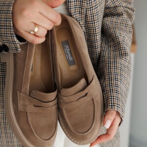 May include: A pair of brown suede loafers with a platform sole. The loafers have a simple design with a single strap across the top. The brand name "Kravet's" is printed on the inside of one of the loafers.