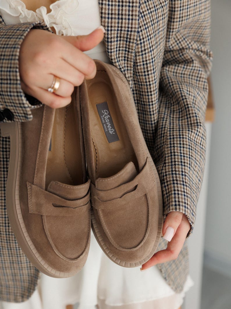 May include: A pair of brown suede loafers with a platform sole. The loafers have a simple design with a single strap across the top. The brand name "Kravet's" is printed on the inside of one of the loafers.