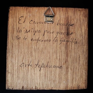 May include: A wooden plaque with a handwritten message in Spanish. The message reads "El  Creador bendise la Milpa para que no se le enferme la familia.  Arte Tepichana."