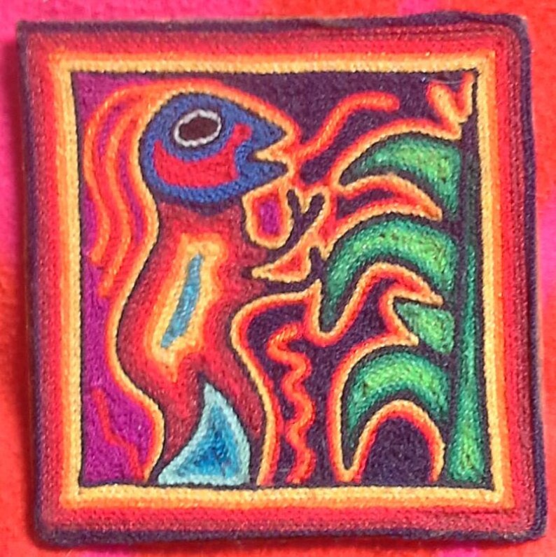 May include: A colorful, hand-stitched artwork depicting a stylized figure with a bird-like head and a plant. The artwork is framed with a multi-colored border.