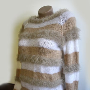 May include: A white and brown striped sweater with a fuzzy texture. The sweater has a crew neck and long sleeves.
