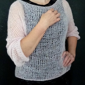 May include: A delicate, light pink knitted sweater with a loose, open-weave pattern. The sweater has a round neckline and three-quarter sleeves.