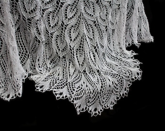 Pode incluir: Um xale branco e rendado com um delicado padrão de folhas. O design intrincado é visível contra um fundo preto. As bordas do xale têm uma borda ondulada, adicionando à sua aparência elegante.