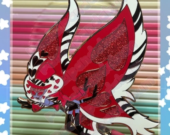 Puede incluir: Un pin de esmalte metálico que muestra un personaje estilizado con grandes alas rojas brillantes en forma de corazón, detalles a rayas blancas y negras y un sombrero rojo. El personaje tiene un rostro pálido, marcas oscuras y una pose dinámica.