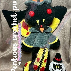 Può includere: Un giocattolo di peluche lavorato a uncinetto a forma di farfalla nera e gialla con occhi rossi e un cappotto grigio. Il giocattolo indossa un papillon nero e ha una coda nera e gialla. Il giocattolo è in piedi su una superficie marrone. Il testo "Sir pentious crochet pattern" è visibile nell'immagine.