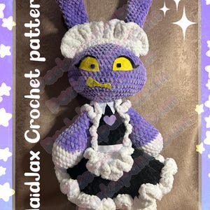 Puede incluir: Muñeca de ganchillo hecha a mano con forma de conejito vestida con un traje de doncella. La muñeca es principalmente morada con detalles blancos y negros. Los ojos son amarillos. El texto "MaidJax Crochet pattern" está en el lado izquierdo.