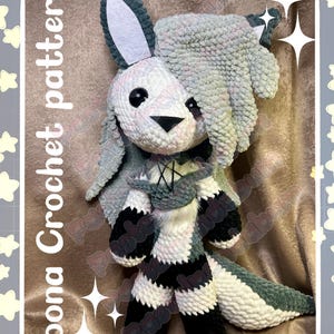 May include: A handmade crochet plushie of a bunny with a white and gray color scheme. The bunny has large ears, black eyes, and a black nose. The plushie has a scarf and striped legs. The text "Loona Crochet pattern" and "Pastelpandabum" are visible.