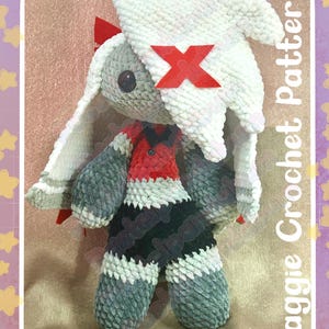 Peut inclure: Poup&eacute;e au crochet faite &agrave; la main avec une t&ecirc;te de lapin blanche, des bras et des jambes gris et une tenue rouge et noire. La poup&eacute;e a un X rouge sur la t&ecirc;te. Le texte "Vaggie Crochet Pattern" et "Pastelpandabum" sont visibles.