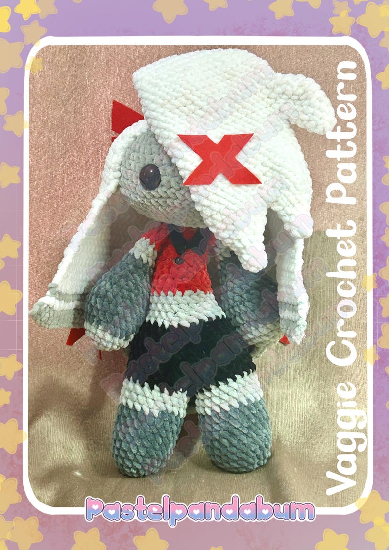 Peut inclure: Poup&eacute;e au crochet faite &agrave; la main avec une t&ecirc;te de lapin blanche, des bras et des jambes gris et une tenue rouge et noire. La poup&eacute;e a un X rouge sur la t&ecirc;te. Le texte "Vaggie Crochet Pattern" et "Pastelpandabum" sont visibles.