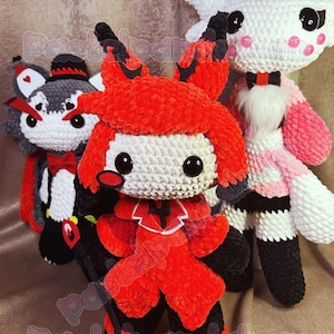 May include: Three crocheted plush toys. One is red with black accents, one is white with pink accents, and one is gray with black accents. All three have large black eyes and white faces.