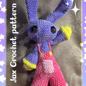 May include: A handmade crochet bunny toy in shades of purple, pink, and yellow. The bunny has large black eyes and is wearing pink overalls with yellow accents. The text "Jax Crochet pattern" is visible on the image.