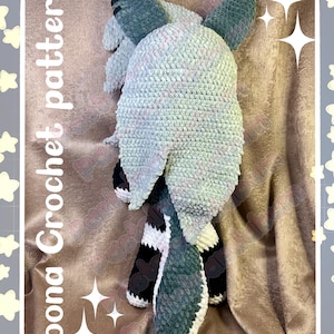 May include: A handmade crochet pattern for a plush animal, featuring a light blue and white body with dark blue ears and a tail. The text "Loona Crochet pattern" and "Pastelpandabum" are visible.