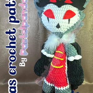 May include: A crocheted plush toy of Stolas from the animated series Helluva Boss. The toy is grey, black, and red with a yellow crown. The toy is standing on a brown surface. "Stolas crochet pattern by pastelpandaum"
