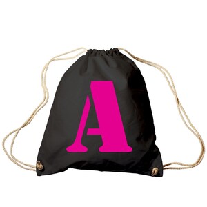 Könnte beinhalten: Eine schwarze Kordeltasche mit einem leuchtend pinkfarbenen Buchstaben "A" auf der Vorderseite.