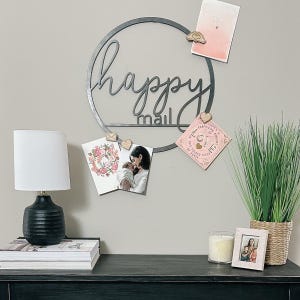 May include: A black metal happy mail sign with a circular frame and a shelf for displaying cards and photos. The sign is decorated with wooden hearts and a pink card with the text "Happy Mail".