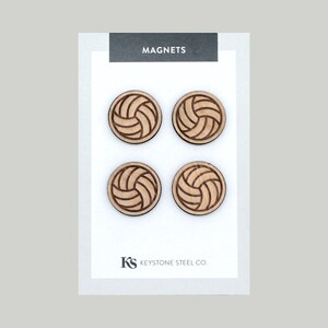May include: Set of four wooden magnets featuring a volleyball design. The magnets are brown and have a natural wood finish. The magnets are packaged on a white card with the text "MAGNETS" and "KEYSTONE STEEL CO."