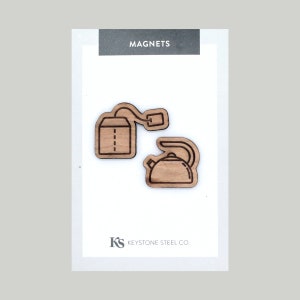 May include: Two wooden magnets, one shaped like a tea bag and the other shaped like a kettle, with the text "MAGNETS" and "KEYSTONE STEEL CO." printed on the card.