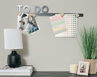 May include: A black metal "To Do" list with wooden hearts and a photo of a family hanging on it. There is a white lamp, a stack of books, a candle, and a framed photo on a black surface.