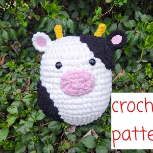 Peut inclure: Patron de crochet pour un jouet en peluche de vache noir et blanc avec un nez rose et des cornes jaunes. Le jouet est assis sur un lit de feuilles vertes.