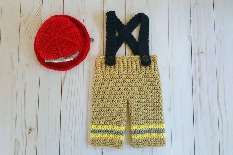 May include: Crocheted firefighter costume for a baby, featuring a red hat and tan overalls with yellow and gray stripes.