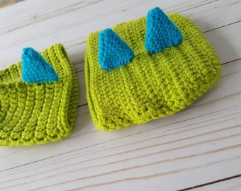 May include: A green and blue crocheted hat and matching headband with pointed ears. The hat and headband are made of soft yarn and are perfect for a baby or toddler.