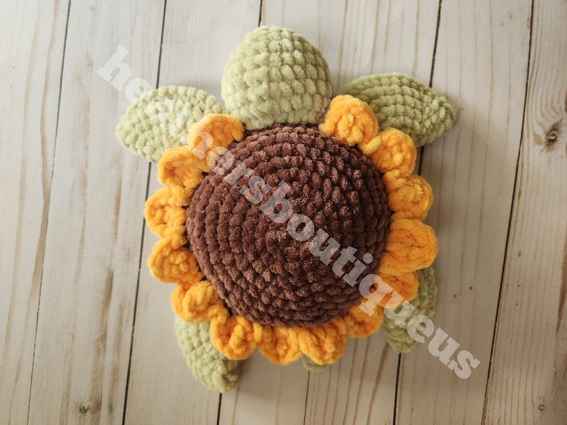 May include: A crocheted sunflower pillow with brown, yellow, and green yarn. The sunflower has a brown center and yellow petals. The leaves are green.