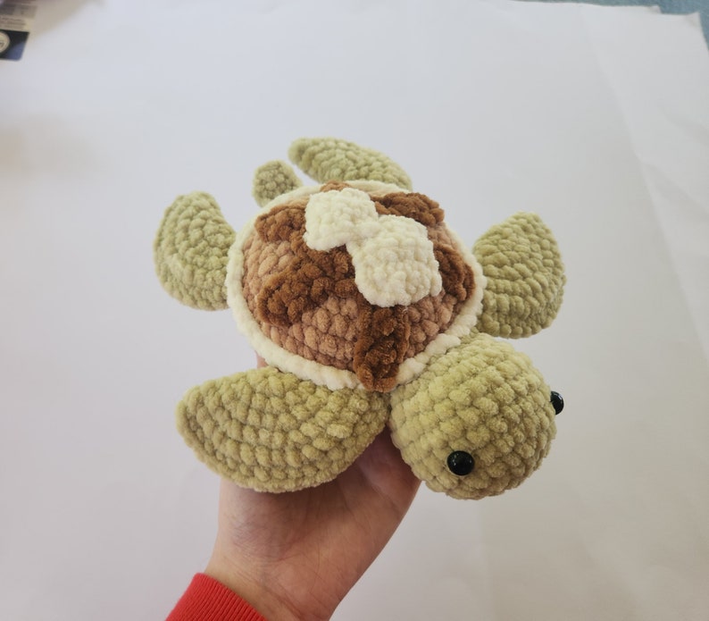 May include: A crocheted plush toy turtle with a brown and white shell and green body. The turtle has black eyes and a soft, fuzzy texture.