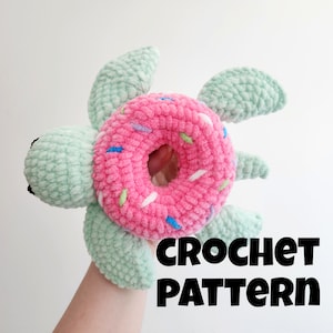 May include: Crochet pattern for a green turtle holding a pink donut with colorful sprinkles. The text "CROCHET PATTERN" is written below the turtle.