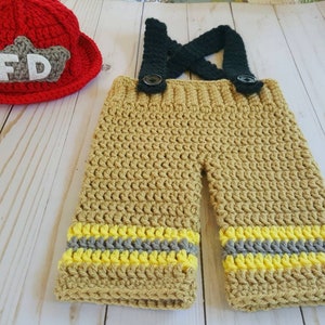 May include: Crocheted firefighter costume for a baby, featuring a red hat with the letters "FD" and tan pants with yellow and gray stripes.