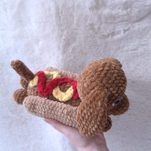 May include: A handmade brown crochet hot dog dog toy with a red and yellow topping. The toy is made of soft, plush yarn and is designed to look like a hot dog. The dog toy is a fun and unique item.