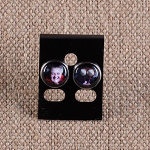 May include: A pair of silver stud earrings with black and white images on the front. The earrings are displayed on a black card.