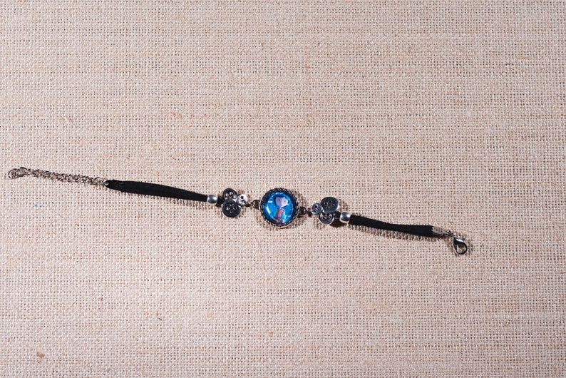 Peut inclure: Un bracelet en cuir noir avec un charme argent&eacute; repr&eacute;sentant un personnage de dessin anim&eacute; bleu et blanc. Le bracelet est dot&eacute; d'un fermoir argent&eacute;.