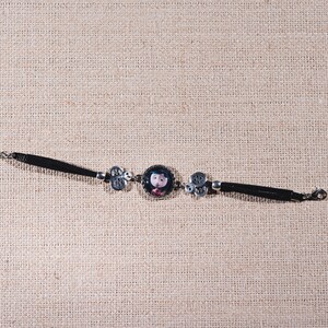 Peut inclure: Un bracelet en cuir noir avec une cha&icirc;ne argent&eacute;e et un charme rond repr&eacute;sentant une fille de dessin anim&eacute;. Le charme est entour&eacute; de deux charmes argent&eacute;s &agrave; motif floral.